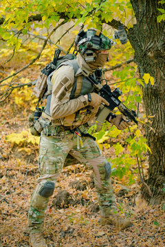 Airsoft man in uniform beside tree move with machine gun. Side view. Vertical photo