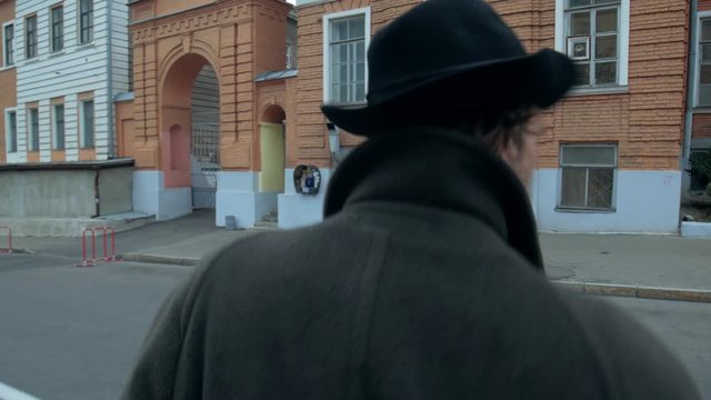 man in a coat and hat crosses expensively across the street in the old town