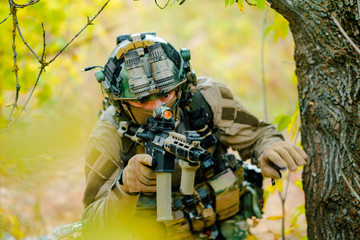 Closeup airsoft man in uniform with machine gun move through the forest. Soldier aims at the sight