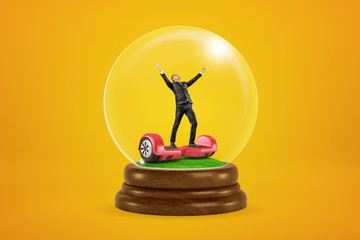 Happy businessman raising arms on red hoverboard in a snow globe on yellow background