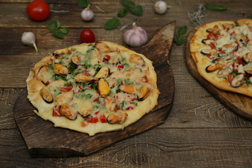 two seafood pizzas with mussels and mozzarella cheese isolated on a wooden board and on a wooden rustic table. Mediterranean food. Vegetarian. 