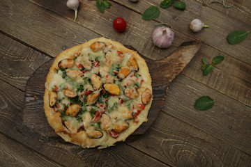 seafood pizza with mussels and mozzarella cheese isolated on a wooden board and on a wooden rustic table. Mediterranean food. Vegetarian. Flat lay. Top view. With copy space for text. 
