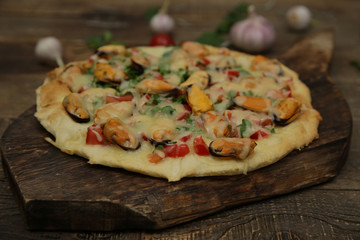 seafood pizza with mussels and mozzarella cheese isolated on a wooden board and on a wooden rustic table. Mediterranean food. Vegetarian. Close-up.