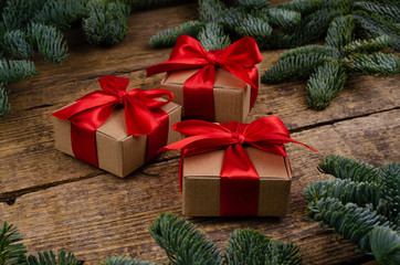 Fototapeta na wymiar Side view of three handmade boxes with bright red ribbons on a wooden background with vibrant Christmas tree branches.