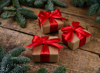 Fototapeta na wymiar Side view of three brown paper boxes with bright red ribbons on a wooden background with green Christmas tree branches.