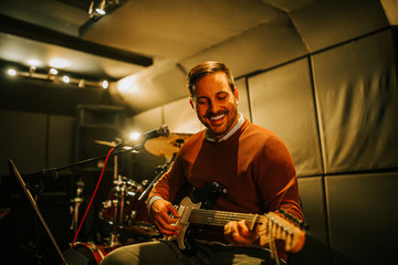 Fototapeta premium Portrait of a handsome smiling man playing electric guitar in recording studio.