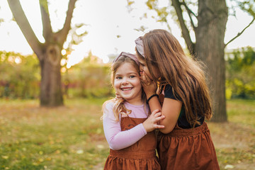 Little girl telling a secret to her young sister. - obrazy, fototapety, plakaty