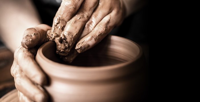 Hands of potter making clay pot on black background