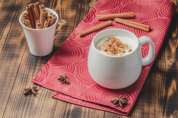 Eggnog. Traditional christmas cocktail in a white mug with cinnamon sticks  and anise on a red napkin. Wooden background.