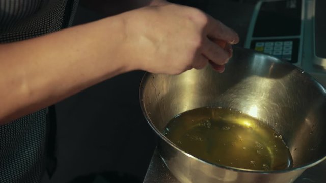 Woman takes eggs from carton holder, separates whites from yolks fast, pouring egg whites into stainless steel bowl. Female hands crack eggshell, then throw it in bin under working table.