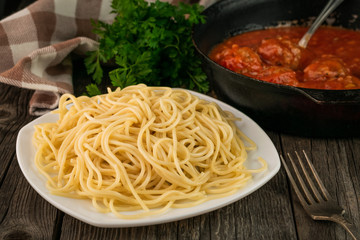Close up spaghetti in a plate and a pan with meatballs in tomato sauce on a rustic wooden background