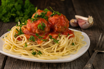 Close-up of American spaghetti with meatballs and tomato sauce with garlic and onions on a rustic wooden background