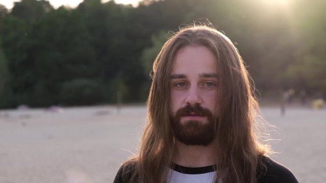 Close up, Portrait of a handsome Caucasian bearded young man with long hair looking artistic at camera in the sunset.