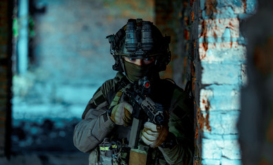 Man in uniform with machine gun and night-vision device stand beside broken wall. Closeup airsoft soldier in night building. Vertcal photo