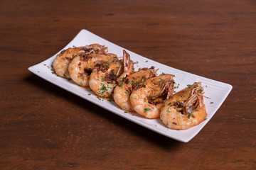 Spicy garlic chili prawns shrimps on white plate isolated over wooden background.