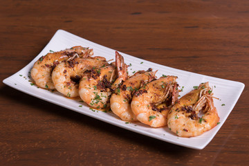 Spicy garlic chili prawns shrimps on white plate isolated over wooden background.