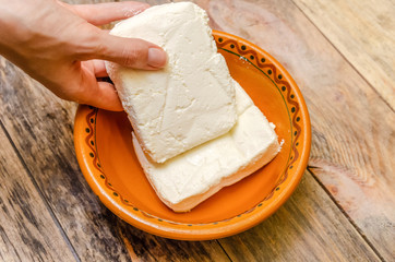 Female hands put a pack of cottage cheese in a clay bowl on a wooden background