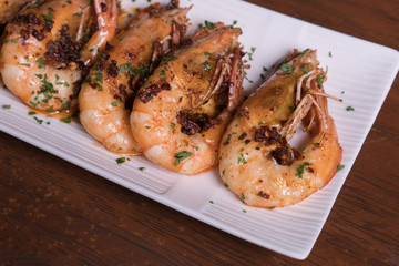 Spicy garlic chili prawns shrimps on white plate isolated over wooden background.