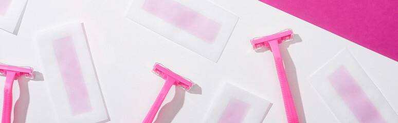 Fototapeta premium top view of disposable razors and wax depilation stripes on white and pink background, panoramic shot