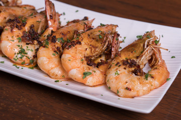 Spicy garlic chili prawns shrimps on white plate isolated over wooden background.