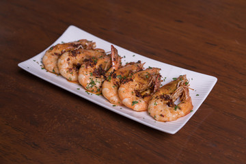 Spicy garlic chili prawns shrimps on white plate isolated over wooden background.