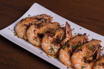 Spicy garlic chili prawns shrimps on white plate isolated over wooden background.
