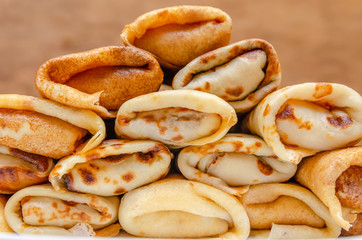 Pancakes with filling stacked pyramid on a white plate, standing on a wooden background close-up