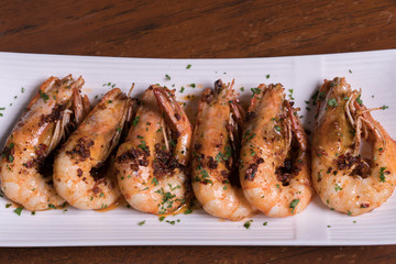 Spicy garlic chili prawns shrimps on white plate isolated over wooden background.