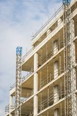 Cranes spanning a large tall high rise construction project before walls have been built onto the structure. Blue but slightly cloudy skies fill the background and it is unknown how tall 