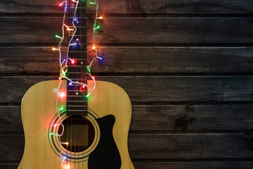 Acoustic guitar in a New Year's garland, guitar in a garland under a wooden wall, copy spaсe	