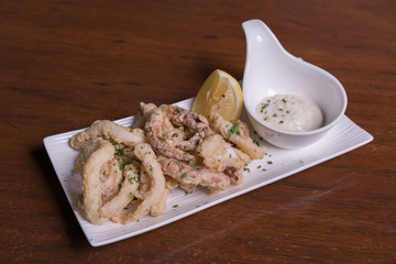 Simple white plate with fresh fried calamari with dipping sauce and slices of lemon, isolated over...