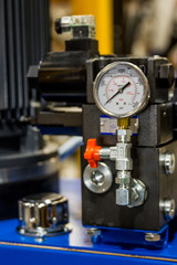 This industrial pressure sensor in a factory is on top a blue box machine used in conveyer systems. This tool helps workers and machinists use their equipment safely.