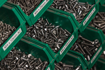 Hundereds of bolts and nuts of various shapes and sizes in green tubs located in a london factory. Used for industrial and commercial production shiny new hardware.
