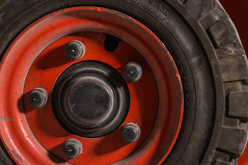 Obraz na płótnie Canvas Red dirty forklift wheel in a factory with dirty tyres and dirty nuts and bolts. Vivid bright colours and dirty tyres. Covered in dust and grime