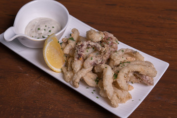 Simple white plate with fresh fried calamari with dipping sauce and slices of lemon, isolated over wooden background.