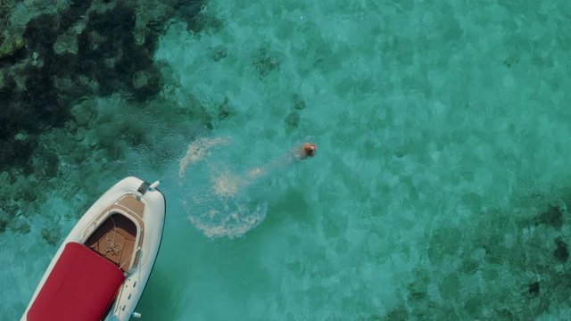 Aerial view of a woman jumping from a boat in a crystal clear water. Luxury travel destination and fantastic nature in the summertime. 
