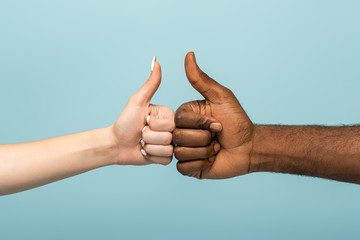 cropped view of interracial couple showing thumbs up isolated on blue