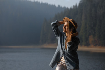 happy young woman in hat enjoys lake view in forest. Relaxing moments. View of stylish girl enjoys the freshness outdoor. Freedom, people, lifestyle, travel and vacation