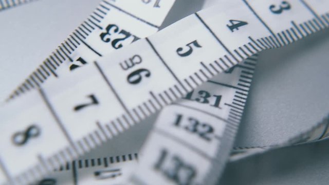 long white soft plastic measuring tape with calibrated in centimeters lies on light grey surface extreme close view
