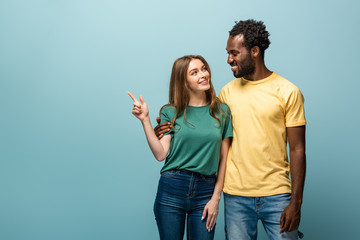 smiling interracial couple pointing with finger away on blue background