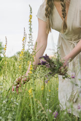 Girl with braids in a beige linen dress picks flowers in the field