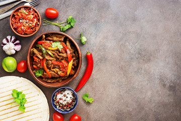 Traditional mexican food fajitas and salsa sauce on a dark rustic background. View from above, flat lay, copy space.