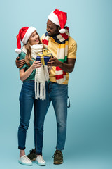 happy african american man in santa hat and scarf gifting present to girlfriend