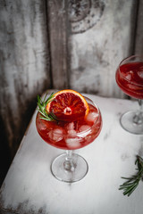 cocktail drink with blood orange and ice decorated with basil on white wooden stool