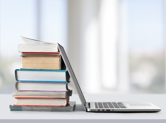 Stack of books with silver laptop on table