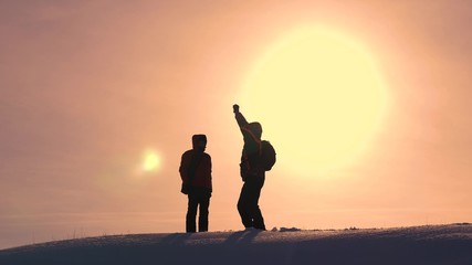 Teamwork concept and winning business. Travelers meet on a snowy hill and rejoice at the victory against the backdrop of beautiful yellow sun. teamwork of people in difficult conditions.