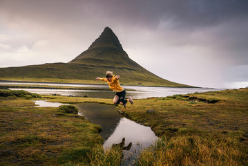 Jonge wandelaar springt over een beekje op de berg Kirkjufell in IJsland