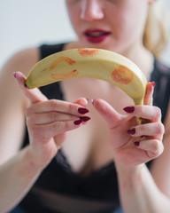 Blonde holds an unpeeled banana with red lipstick marks. The concept of oral sex. Seductive look....