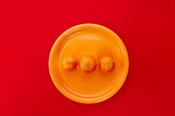 Tangerines on orange plate. Monochrome styled flat lay on bold red background.