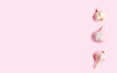 Three heads of fresh garlic on a pink background, top view